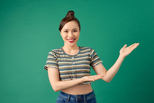 Happy smiling young Asian woman showing blank area for sign or copyspace, isolated over green background.