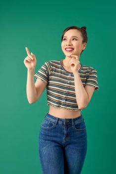 Portrait of young Asian woman pointing her finger and look around over green background.