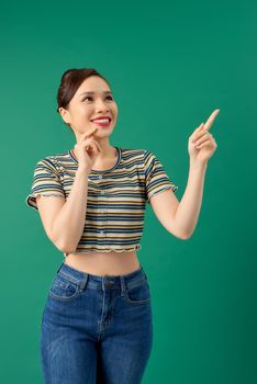 Smiling happy young Asian woman pointing her hand over green background.