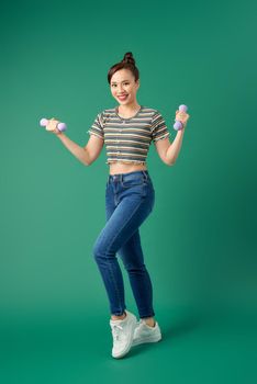 Full-length of young Asian woman holding dumbell over green background.