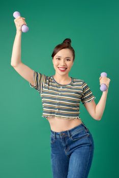 Smiling attractive young Asian woman practicing exercise with dumbell over green background.