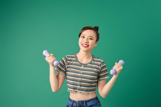 Smiling attractive young Asian woman practicing exercise with dumbell over green background.