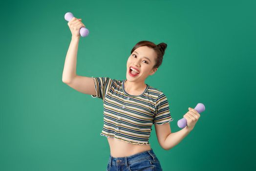 Young Asian woman holding dumbell and wearing casual clothing over green background.