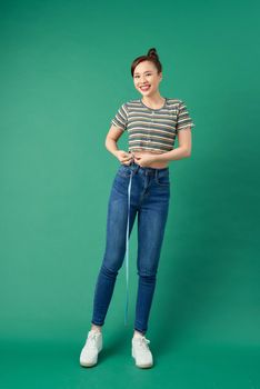 Beautiful young Asian woman measuring her waist with a measure tape over green background.