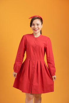 Full length of beautiful young Asian woman wearing red dress and standing over orange background
