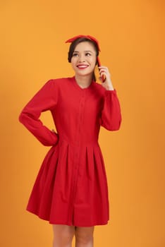 Young Asian Girl using smartphone while standing over orange background