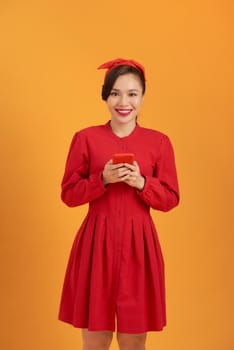 Portrait of happy young Asian woman using phone isolated over orange background.