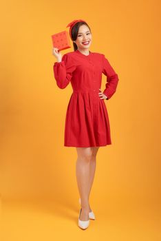 Happy young Asian woman holding gift box isolated over orange background.