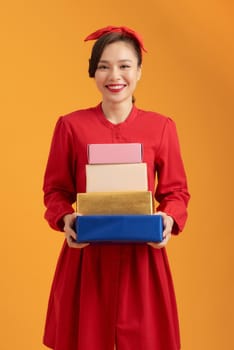 Portrait of a cute young girl in dress holding stack of present boxes isolated over orange background