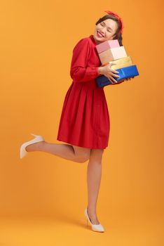 Smiling young Asian lady holding gift boxes isolated over orange background.