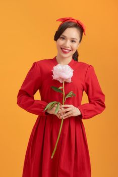 Portrait of happy young Asian woman holding peony flower over orange background.