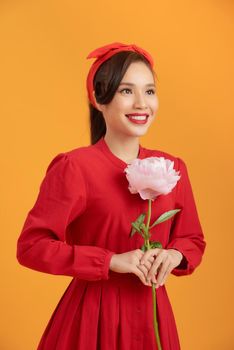 Close up young Asian woman holding peony flower over orange background.