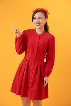 Beautiful young Asian woman pointing her hand and standing isolated over orange background.