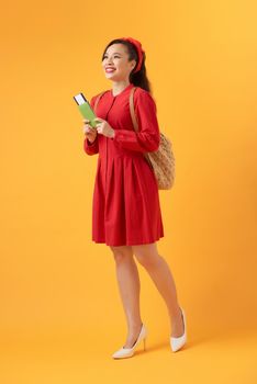 Young Asian woman wearing backpack and holding flight ticket over orange background