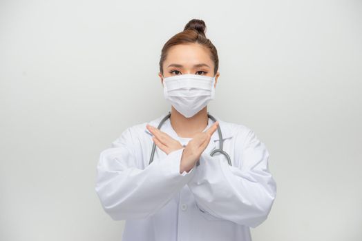 A young beautiful woman doctor in a white coat shows a stop gesture on white background. Say No virus disease.