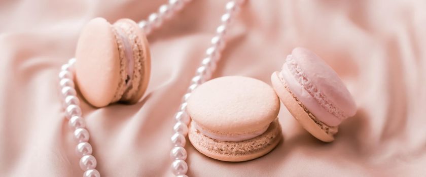 Girly, bakery and branding concept - Sweet macaroons and pearls jewellery on silk background, parisian chic jewelry, French dessert food and cake macaron for luxury confectionery brand, holiday gift