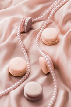 Girly, bakery and branding concept - Sweet macaroons and pearls jewellery on silk background, parisian chic jewelry, French dessert food and cake macaron for luxury confectionery brand, holiday gift