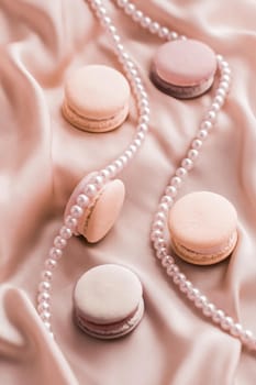 Girly, bakery and branding concept - Sweet macaroons and pearls jewellery on silk background, parisian chic jewelry, French dessert food and cake macaron for luxury confectionery brand, holiday gift