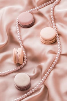 Girly, bakery and branding concept - Sweet macaroons and pearls jewellery on silk background, parisian chic jewelry, French dessert food and cake macaron for luxury confectionery brand, holiday gift