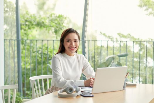 Single happy female business owner with smile on phone and working on laptop computer at desk with bright window in background