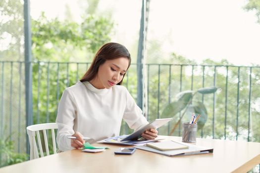 Beautiful asian girl smiling looking at tablet near big window. Copy space