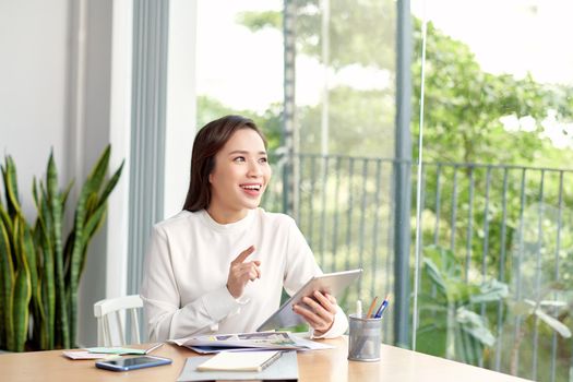 Smiling young woman reading something on the tablet and sitting near the windowsill at home