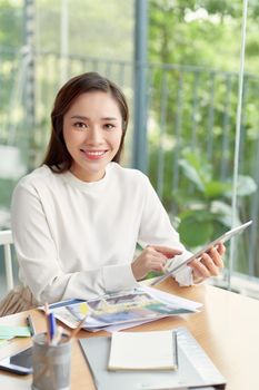 Happy young Asian woman sitting at table in her dining room making notes, selective focus