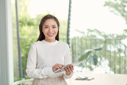 Attractive businesswoman using a digital tablet while standing in front of windows in an office building