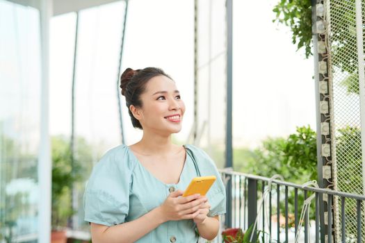 Young Asian woman enjoying nature and using phone on the balcony