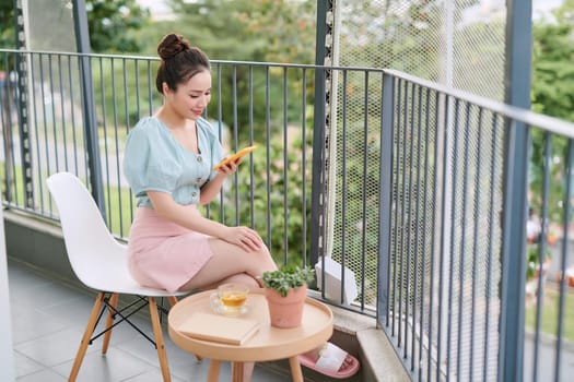 Beautiful girl having breakfast in the balcony, while using her phone.