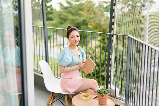 Young attractive Asian girl reading a book on balcony.