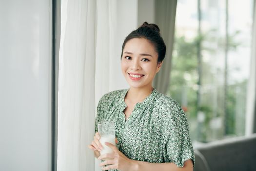 Asian lady drinking glass of milk while looking out the window with copy space