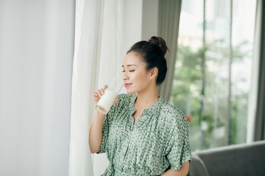 Happy young Asian woman drinking milk from the glass  in the living room at home