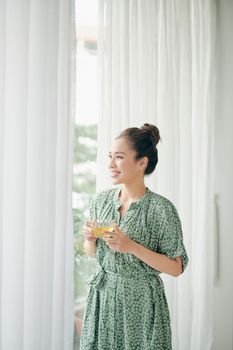 Beautiful Young Woman near big Window holding cup and relax inside home
