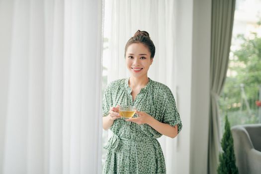 Beautiful young woman is looking out the window and holding a cup of tea