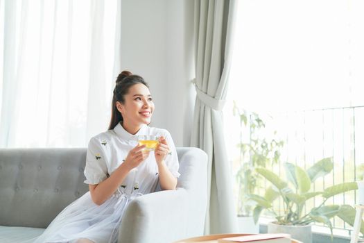 Positive young attractive woman in her room holding and enjoying a cup of tea