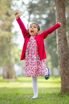 Little girl in flower dress and red sweater, very happy and smiling in the forest