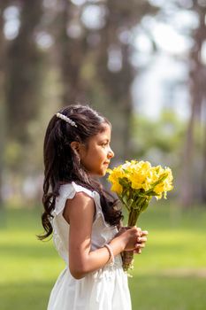 Little girl in white dress and with a cute bouquet of flowers in her hand
