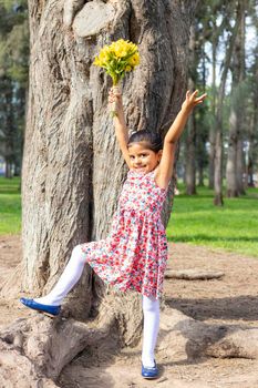 Little girl in dress celebrating in the park with a bouquet of flowers in her hand