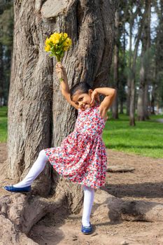 Little girl in dress celebrating in the park with a bouquet of flowers in her hand