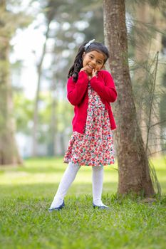 Little girl in flower dress and red sweater, very happy and smiling in the forest