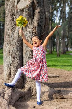 Little girl in dress celebrating in the park with a bouquet of flowers in her hand