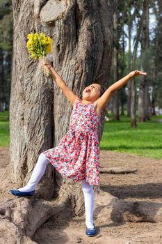 Little girl in dress celebrating in the park with a bouquet of flowers in her hand