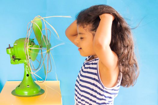 Beautiful girl, is cooling off the heat with an old green fan