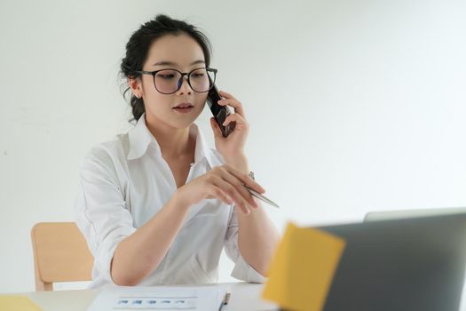 Busy Business woman discuss with cilent by video call and talking with cell phone. female technical support agent trying to explain something to a client while working on laptop at call center