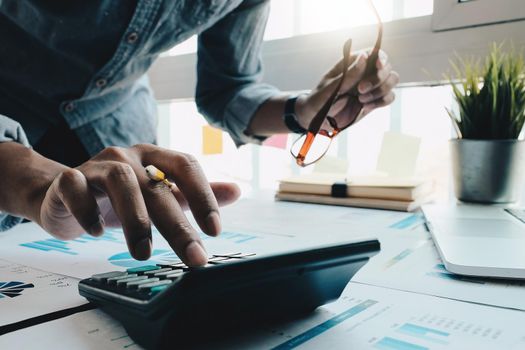 Close up of businessman or accountant hand holding pencil working on calculator to calculate financial data report, accountancy document and laptop computer at office, business concept.