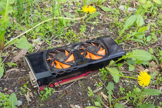 An old and broken computer video card after bitcoin mining, thrown into the street, lies in the grass and pollutes nature