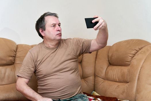 Senior citizen sitting on the couch understands the gadget. Pensioner takes a selfie on a smartphone