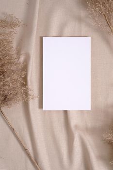 White blank paper card mockup with pampas dry grass on a beige neutral colored textile