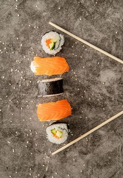Japanese cuisine. Traditional japanese sushi placed between chopsticks on dark background. Top view. Flat lay